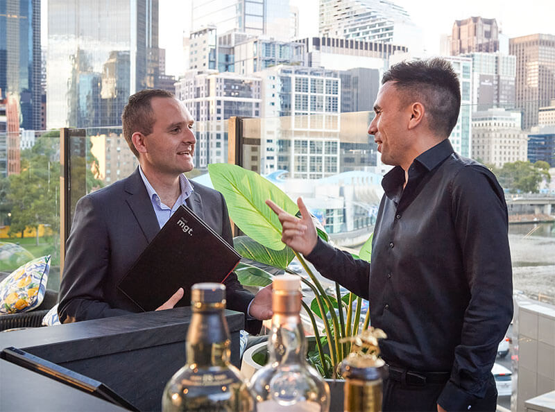 2 men in dark suits having a discussion at a bar in the city