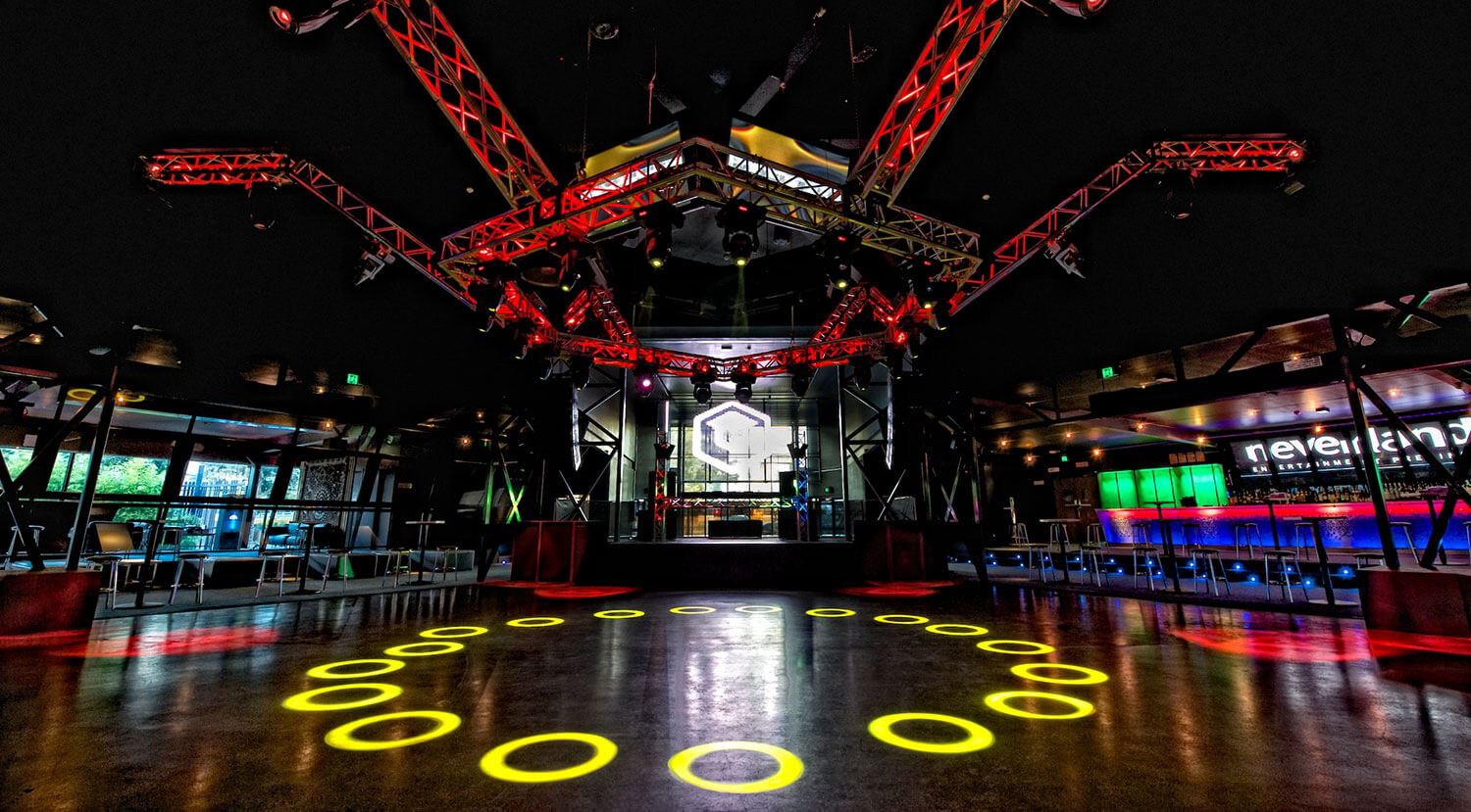 Empty nightclub view of dance floor with colourful lights coming from DJ booth