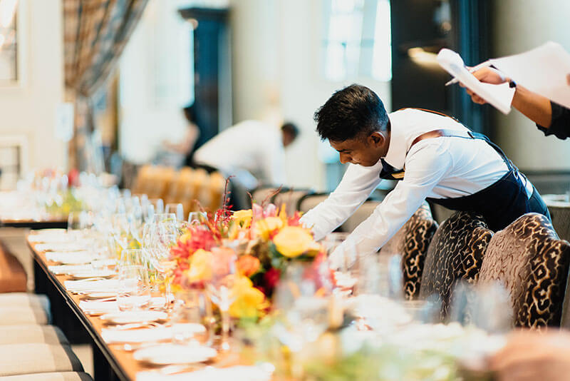 A waiter preparing a table setting in a busy restaurant